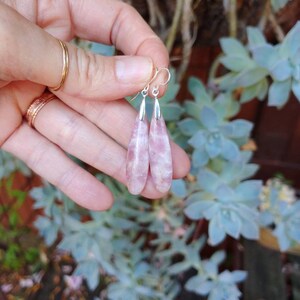 Op de afbeelding: Een paar oorhangers met roze en witte traanvormige stenen. De stenen zijn gezet in zilver.