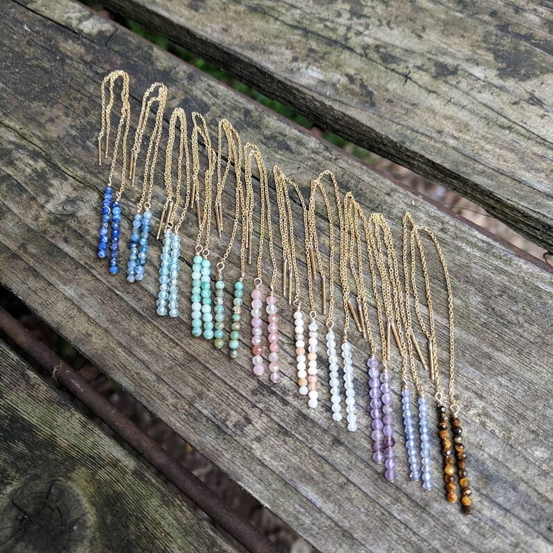 May include: A set of 12 pairs of beaded dangle earrings with gold chains. The beads are in a rainbow of colors, including blue, green, pink, white, purple, and brown.