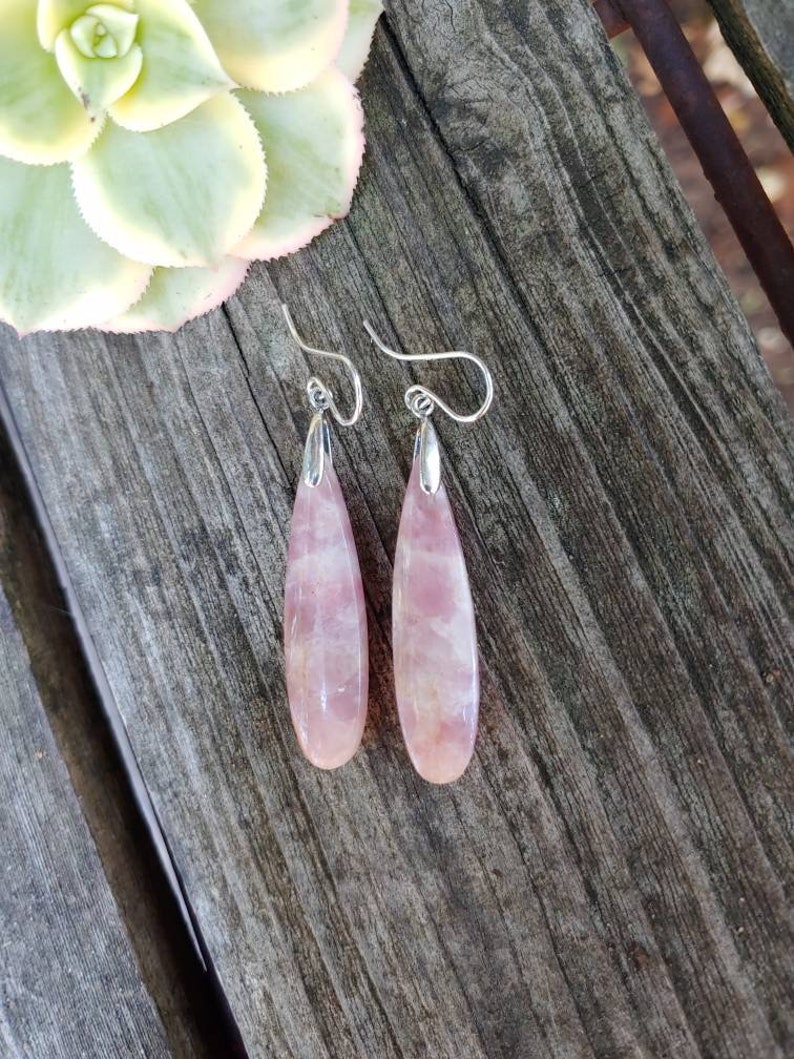 Op de afbeelding: Een paar oorbelletjes met roze druppelvormige stenen en zilveren haakjes.