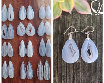 May include: A pair of silver teardrop earrings with blue agate stones. The stones have a natural, raw look with a white and blue color pattern. The earrings are on a wooden surface.