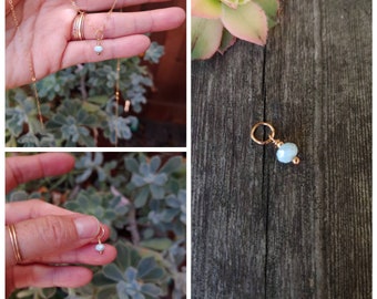 May include: A delicate gold chain necklace with a small light blue gemstone pendant.