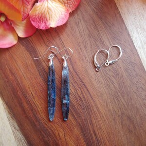 May include: A pair of silver dangle earrings with blue and silver teardrop-shaped stones. The earrings are on a wooden surface.
