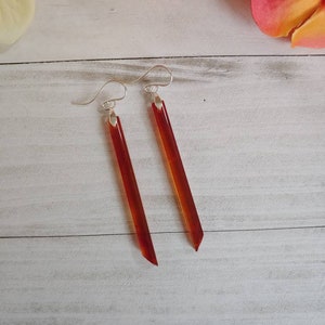 May include: A pair of dangle earrings with long, thin, reddish-brown teardrop-shaped stones. The earrings have silver hooks.