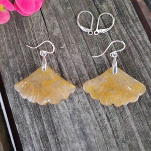Può includere: Un paio di orecchini a forma di foglia di ginkgo giallo con ganci d'argento. Gli orecchini sono realizzati in un materiale translucido con un design delicato a forma di ventaglio.