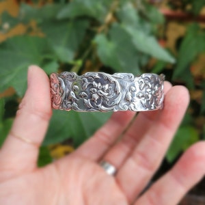 May include: A silver bracelet with a floral design. The bracelet is made from a repurposed spoon.