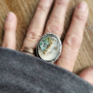May include: A silver ring with a large oval-shaped agate stone. The stone has a white base with brown and green inclusions.