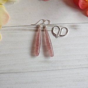 May include: A pair of dangle earrings with a light pink, translucent stone. The earrings are made of silver and have a simple, elegant design.