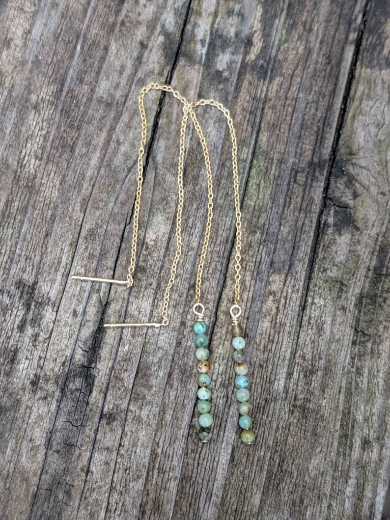 May include: A pair of gold chain earrings with turquoise beads. The earrings are long and dangle.