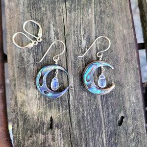 May include: A pair of silver crescent moon earrings with iridescent abalone shell accents and dangling blue gemstone charms.