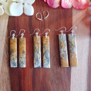 May include: A set of six earrings featuring yellow and brown stone with black veins. The earrings are rectangular in shape and have silver hooks.