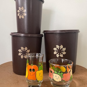 Puede incluir: Un conjunto de recipientes de plástico marrón vintage con tapas, con un diseño floral dorado. Dos vasos de chupito transparentes están decorados con coloridas verduras de dibujos animados, incluyendo pimientos naranjas, amarillos y rosas.