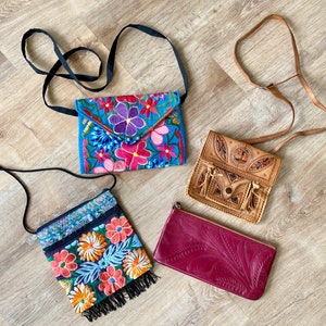 May include: Four bags: a blue envelope-style bag with colourful floral embroidery and a black strap, a rectangular bag with orange and yellow floral embroidery and black fringe, a tan leather bag with intricate tooling, and a red leather clutch.
