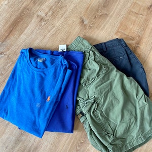 May include: A bright blue t-shirt with an orange logo, a dark blue waffle-knit long-sleeve shirt with a small logo, olive green cargo shorts with side pockets, and a pair of dark navy blue trousers, all featuring the Polo Ralph Lauren brand.