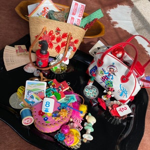 May include: A collection of assorted vintage items including a straw tote with red floral embroidery, a white handbag with a cartoon graphic, a pink leather pouch, playing cards, dice, miniature figurines, spools of thread, and various trinkets.
