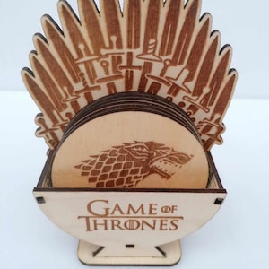 Peut inclure: Un ensemble de six sous-verres en bois sur le thème de Game of Thrones. Les sous-verres sont circulaires et ont une finition en bois brun. Le sous-verre supérieur présente une gravure détaillée du sigle du loup-garou. Les sous-verres sont empilés dans un support en forme de Trône de Fer, avec les mots "Game of Thrones" gravés sur le devant.