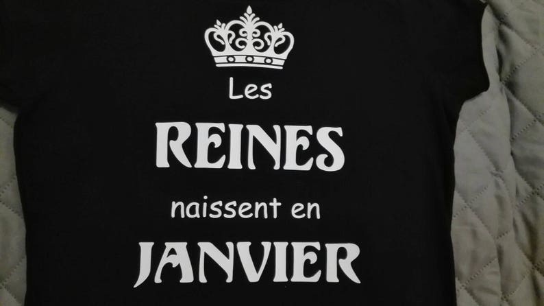 May include: Black t-shirt with white text that reads "Les Reines naissent en Janvier" and a crown graphic.
