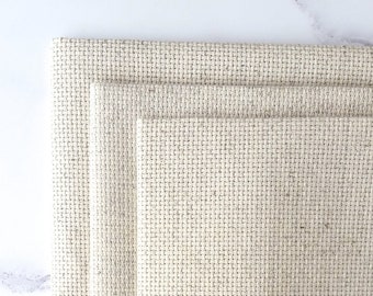 May include: Three pieces of beige Aida cloth, a type of fabric used for cross-stitch embroidery, stacked on top of each other.