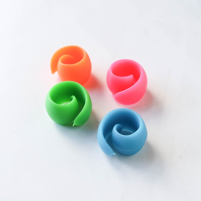 May include: Four colorful silicone wine glass charms in orange, pink, green, and blue. Each charm has a spiral design, perfect for identifying glasses at a party or gathering. These reusable charms are a fun and practical accessory.