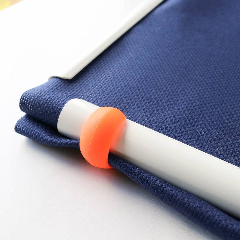 May include: Close-up of a blue fabric with a white bar and an orange ring. The fabric is folded over the white bar. The orange ring is wrapped around the white bar. The background is white.