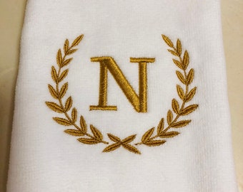 May include: White hand towel with a gold embroidered wreath and the letter N in the center.
