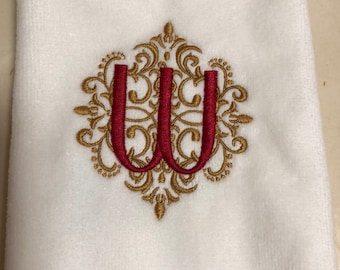 May include: White hand towel with a gold and red embroidered monogram of the letter "W" in a decorative frame.