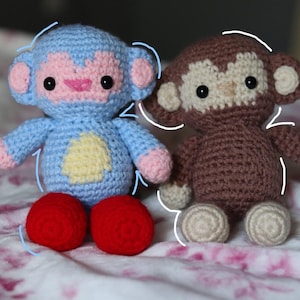 May include: Two crocheted monkey plush toys. The left monkey is light blue with a pink face, ears, and hands, a yellow belly patch, and bright red feet. The right monkey is brown with a beige face, ears, and hands, and beige feet.