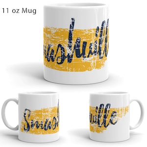 May include: White ceramic 11 oz mug with a yellow and blue design. The design features the word "Nashville" in a distressed blue font on a yellow background.