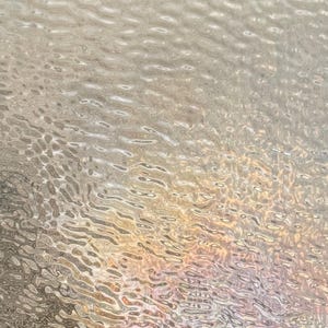 May include: Abstract image of a rippled, textured surface. The surface has a pattern of flowing lines and small, irregular shapes. The colors shift from light beige to pale pink and gold, creating a shimmering effect.