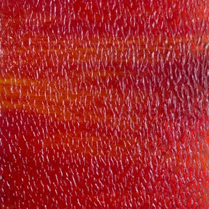 May include: A sheet of translucent red glass featuring a textured surface with a repeating pattern of vertical, elongated, and irregular ridges that create a rippled effect across the entire material, allowing light to pass through the vibrant red color.