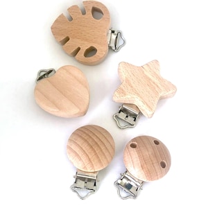 Puede incluir: Cinco mordedores de bebé de madera con clips metálicos. Los mordedores tienen forma de corazón, estrella, hoja y dos círculos. Los mordedores son de color marrón claro.