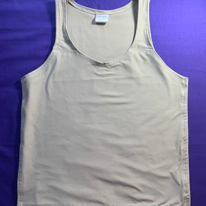 May include: A beige sleeveless tank top featuring a scoop neckline and visible stitched seams along the sides and hem. The garment includes a small white rectangular label at the inner neckline with printed text that is partially visible.