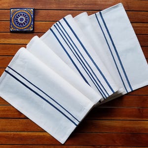 May include: Set of five white table runners with navy blue stripes. The runners are folded and arranged in a fan shape on a wooden surface.