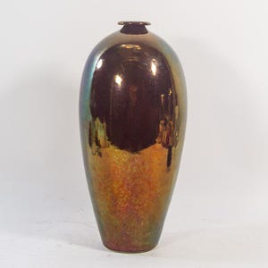 Könnte beinhalten: Eine hohe, schillernde Vase mit rundem Körper und schmalem Hals. Die Vase hat eine metallische Oberfläche mit Farben, die von Bronze über Grün bis Gold reichen. Ein dekoratives Wohnaccessoire.