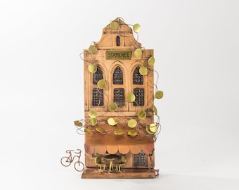 May include: A miniature model of a Dutch building with a brown facade and gold accents. The building has a sign that reads "Stamenee" and is decorated with gold leaves. There are two bicycles parked in front of the building.