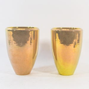 Op de afbeelding: Twee keramische vazen met een metallic gouden en bronzen afwerking. De vazen hebben een afgeronde basis en een licht uitlopende bovenkant. De vazen worden gepresenteerd tegen een witte achtergrond.