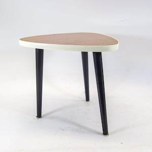 Puede incluir: Una pequeña mesa auxiliar triangular con una tapa de laminado blanco y patas negras. La mesa tiene un diseño único y moderno.