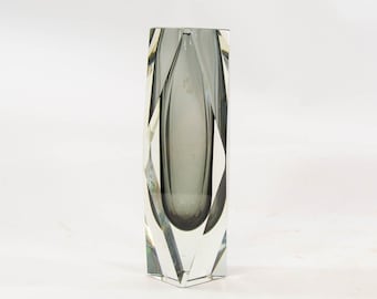 May include: A clear glass vase with a geometric design. The vase is tall and narrow, with a grey interior.