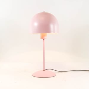 May include: A light pink table lamp featuring a smooth, dome-shaped shade and a slender, matching vertical stem. The lamp stands on a circular base and includes a black and white fabric-covered power cord extending from the base to the side.