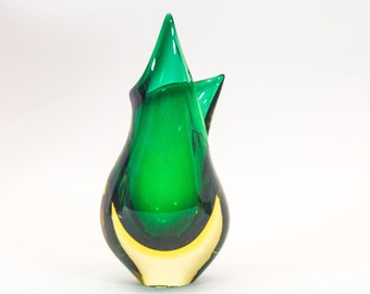 May include: A green glass vase with a yellow base. The vase has a unique, abstract shape with a pointed top.