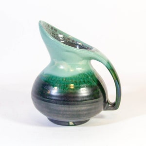 Peut inclure: Un pichet en céramique vert et bleu avec une poignée incurvée unique. Le pichet a une finition émaillée et une surface légèrement texturée.