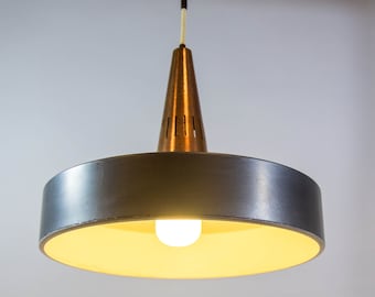 May include: A silver and brass pendant light with a round, flat shade and a cone-shaped top. The light is on and illuminating the room.