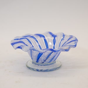May include: A small, clear glass bowl with blue and white stripes. The bowl has a ruffled edge and a small, clear glass base.
