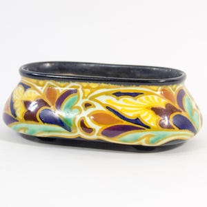 Peut inclure: Un plat ovale en céramique avec un bord et une base bleu foncé. Le plat est décoré d'un motif floral jaune, orange, violet et vert. Le design est symétrique et détaillé, avec une finition brillante.