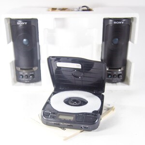 May include: A black Sony CD player with a white disc inside and two black Sony speakers on either side. The speakers are in white boxes with the word "SONY" printed on them.