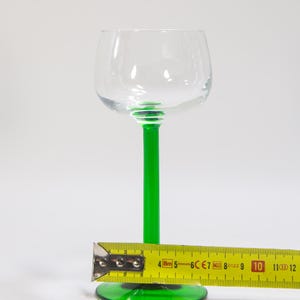 May include: A clear glass wine glass with a green stem and base. The glass is approximately 25 cm tall.