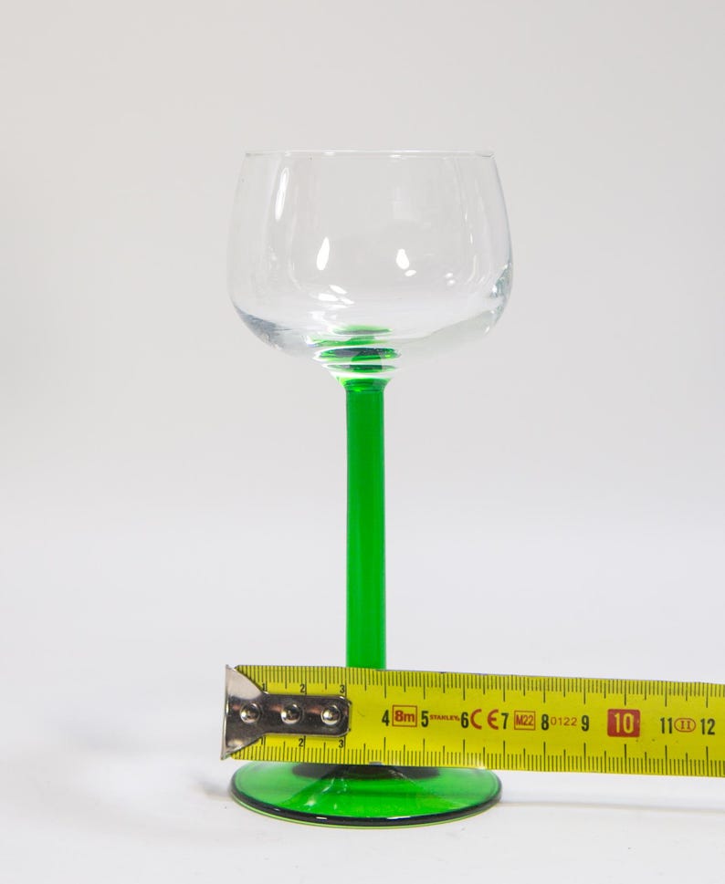 May include: A clear glass wine glass with a green stem and base. The glass is approximately 25 cm tall.