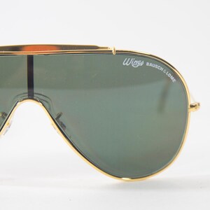 May include: Gold-tone aviator sunglasses with green lenses and the text "Wings Bausch & Lomb" on the frame.