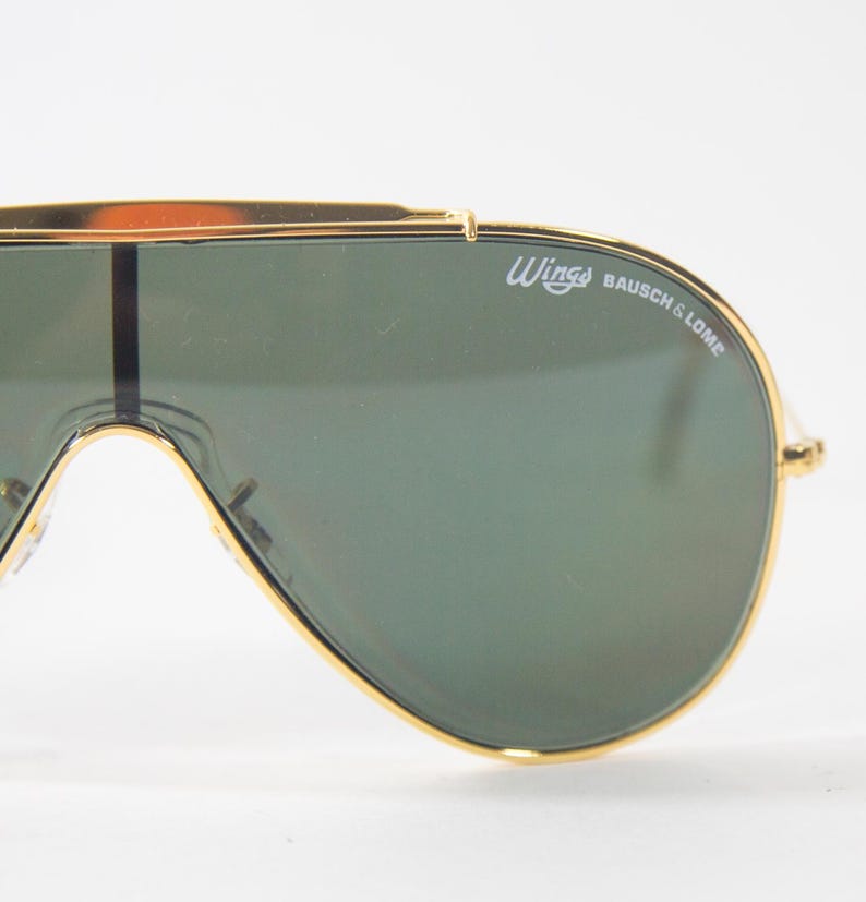 May include: Gold-tone aviator sunglasses with green lenses and the text "Wings Bausch & Lomb" on the frame.
