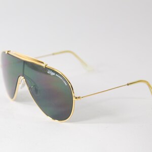 May include: Gold-framed aviator sunglasses with green lenses. The sunglasses have a 'W' logo on the frame.
