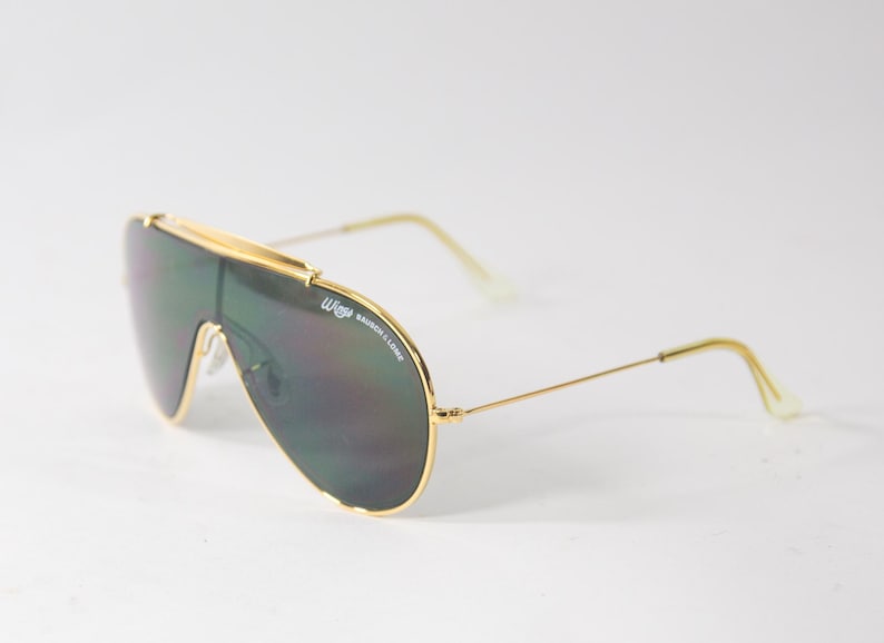 May include: Gold-framed aviator sunglasses with green lenses. The sunglasses have a 'W' logo on the frame.